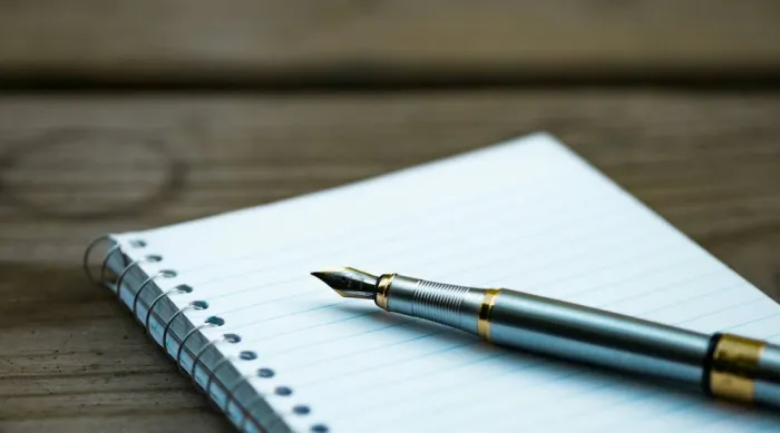 A fountain pen resting on a clean lined notepad on a wooden surface