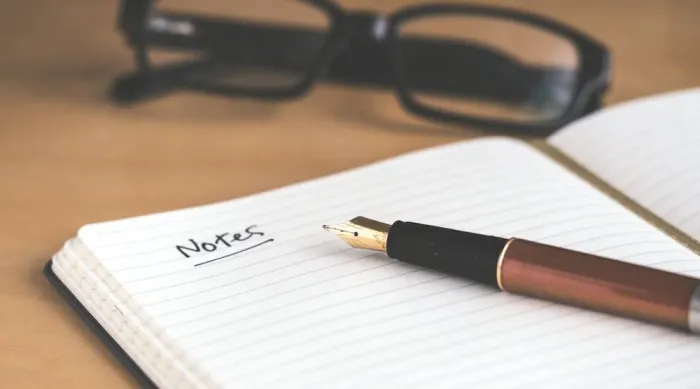 An open notebook with the word Notes written in fountain pen beside reading glasses